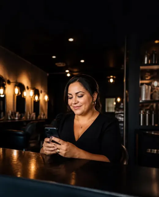 Dueña de un salón sonriendo al ver una cita confirmada en su celular